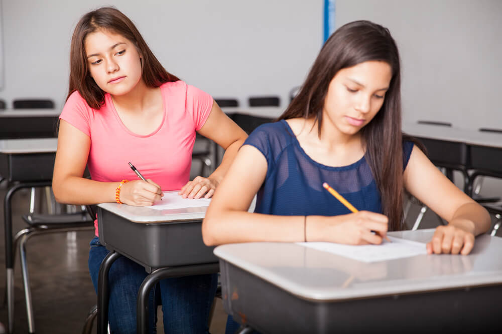 two girls taking a test with one looking over the shoulder of the other for the answers