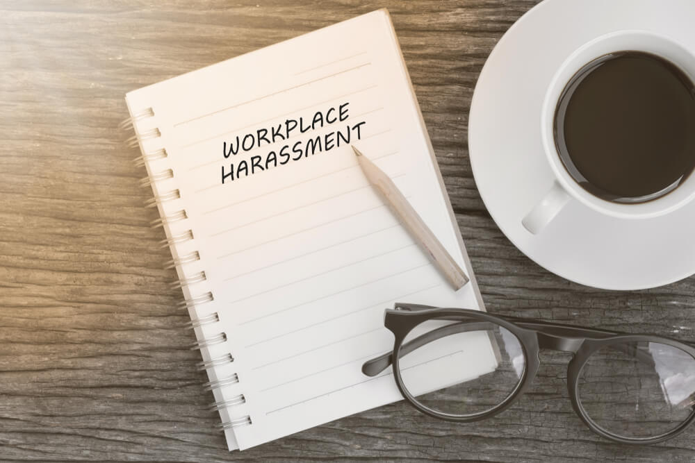 Workplace harassment concept on notebook with glasses, pencil and coffee cup on wooden table